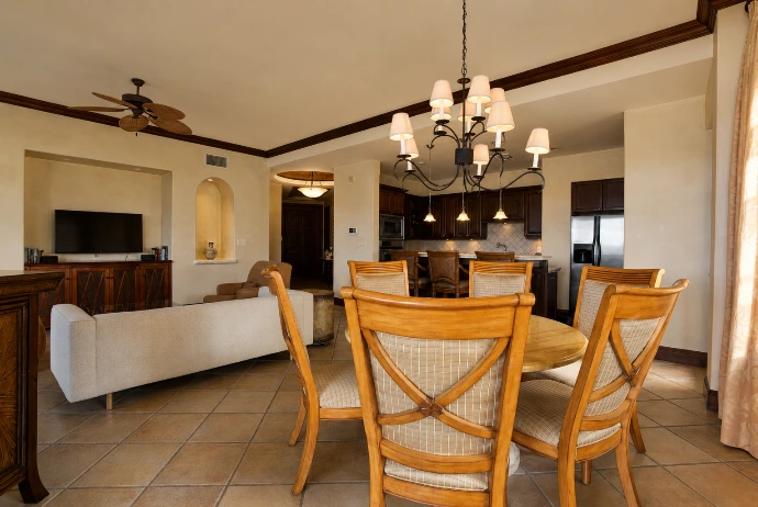 Open-plan dining and living area at Marbella 6D, featuring warm wood furnishings, a statement chandelier, and an adjoining kitchen at Los Sueños Resort.