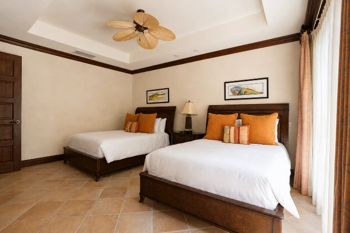 Window-side view of the double guest bedroom at Marbella 6D, featuring two beds, tropical-inspired artwork, and warm natural light at Los Sueños Resort.
