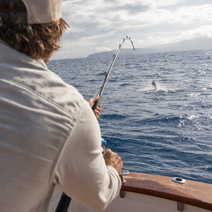 A guest fishing from a private sportfishing charter off the Pacific coast of Los Sueños, Costa Rica, with a sailfish breaking the surface in the distance.