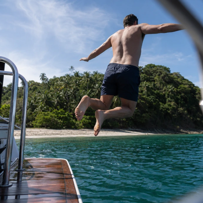 A guest jumps from a private yacht into the clear Pacific waters beside the tropical shoreline of Tortuga Island, Costa Rica.