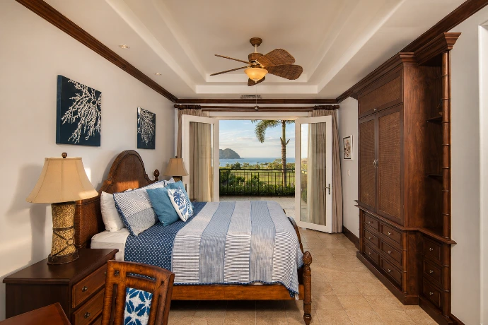 Elegant primary bedroom at Villa Tranquila featuring rich wood finishes, refined blue accents, and panoramic Pacific Ocean views in Vista del Sol at Los Sueños Resort, Costa Rica.