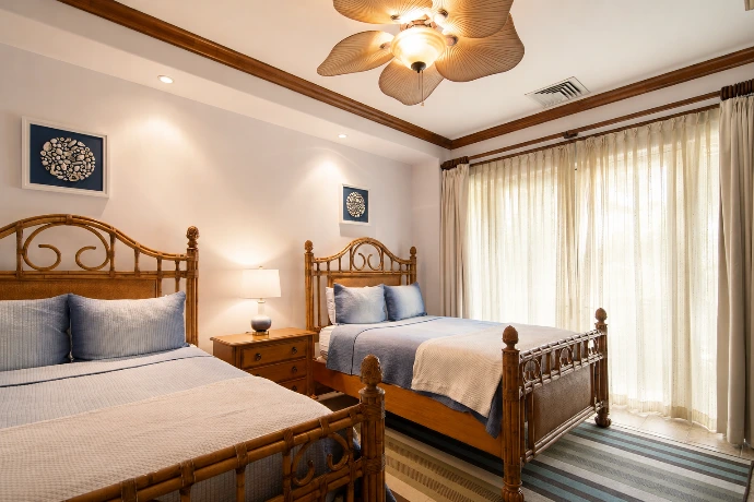 Spacious guest bedroom at Villa Tranquila featuring two beds, elegant wood finishes, soft blue textiles, and refined tropical design in Vista del Sol at Los Sueños Resort, Costa Rica.