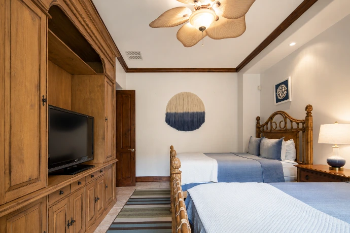 Spacious guest bedroom at Villa Tranquila featuring two queen-size beds, custom wood cabinetry, soft blue textiles, and refined tropical design in Vista del Sol at Los Sueños Resort, Costa Rica.