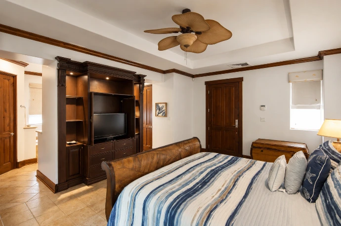 Spacious guest bedroom at Villa Tranquila featuring custom wood cabinetry, a private entertainment center, refined blue textiles, and tropical-inspired design in Vista del Sol at Los Sueños Resort, Costa Rica.