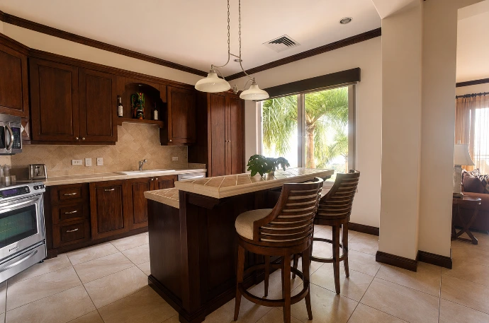 Fully equipped kitchen at Altavista 1A featuring rich wood cabinetry, stainless steel appliances, a breakfast bar, and warm natural light at Los Sueños Resort, Costa Rica.