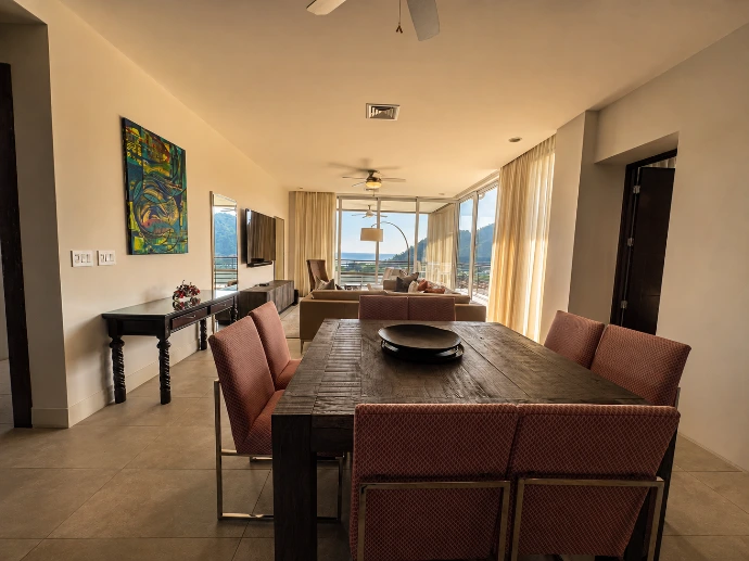 Open-concept dining and living area at Montecielo 5A, with floor-to-ceiling windows overlooking the Pacific Ocean and tropical hills of Los Sueños, Costa Rica.