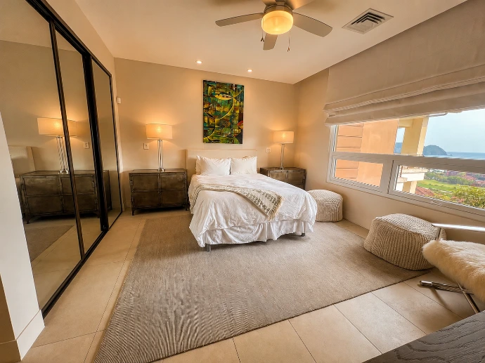 Guest bedroom at Montecielo 5A featuring contemporary coastal décor, mirrored closets, abundant natural light, and Pacific Ocean views in Los Sueños, Costa Rica.