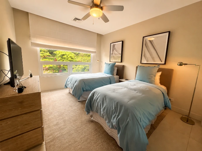 Twin bedroom at Montecielo 5A featuring two individual beds, soft blue bedding, contemporary décor, and lush tropical views in Los Sueños, Costa Rica.