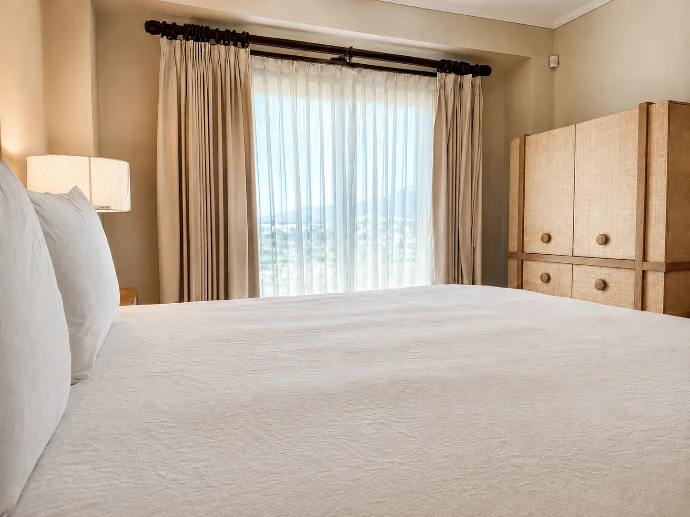 Primary bedroom with white bedding, a large curtained window, and a wood cabinet at Del Mar 4D in Los Sueños Resort.