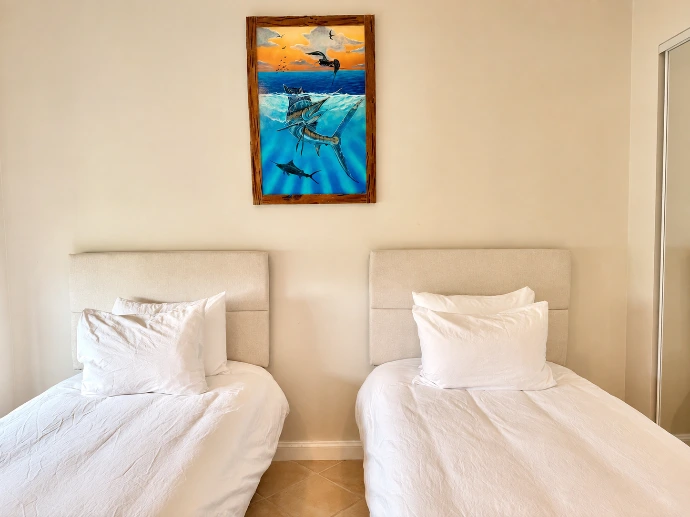 Twin guest bedroom with two single beds and framed sportfishing artwork at Del Mar 4D in Los Sueños Resort.