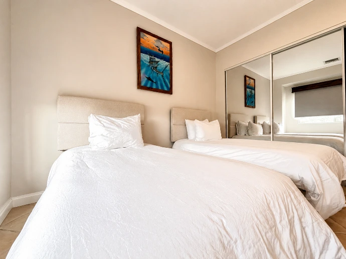 Twin guest bedroom with two single beds, mirrored closet doors, and sportfishing artwork at Del Mar 4D in Los Sueños Resort.
